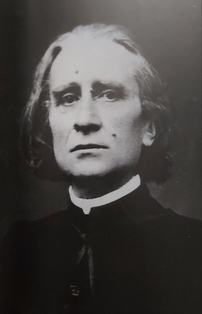 Picture in black and white taken in 1866. Liszt wears a cassock and looks at the camera with a serious face. Only his shoulders and his head can be seen.
