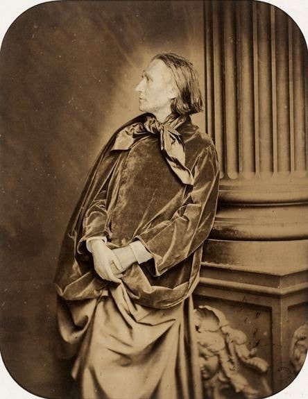 Picture in black and white taken in 1861, showing Liszt in front of a greek column. Liszt is drapped in a large piece of fabric and wears a scarf.
