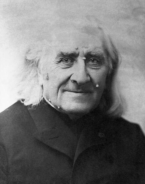 Picture in black and white taken in 1885, showing Liszt wearing a black coat. He has long white hair. He is facing the camera and smiling.
