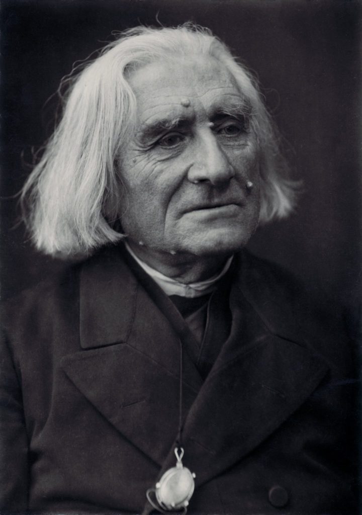 Picture in black and white taken in 1884. It represents Liszt wearing a black cassock and a black coat. His glasses are attached to one of the buttons. Only his head and his shoulders can be seen. He looks toward his left and smiles slightly.