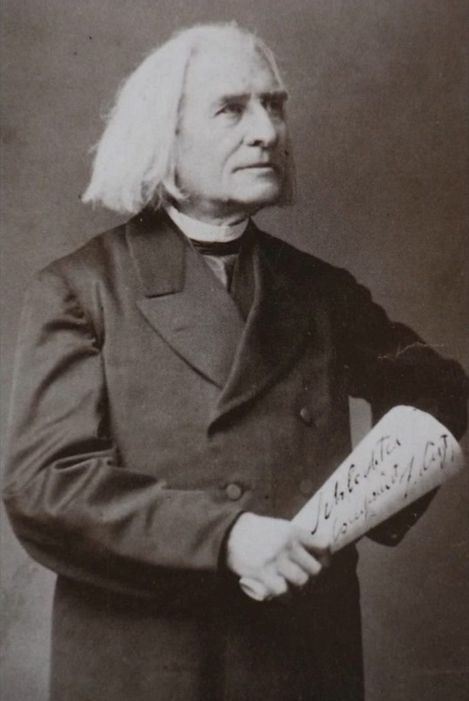 Picture in black and white taken in 1881. It represents Liszt standing, wearing a black cassock and a black coat. He looks toward his left and smiles. He has a score in his right hand, on which something is written in German. It says: bad composer.