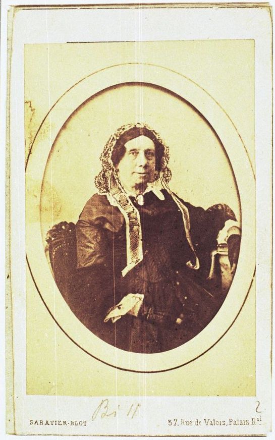 Picture in yellow and white, taken in 1860. It represents Anna Liszt, Franz Liszt's mother. She wears a black dress and has a white bonnet on his head. She looks at the camera and smiles. The name and address of the photographer can be seen at the bottom of the picture.