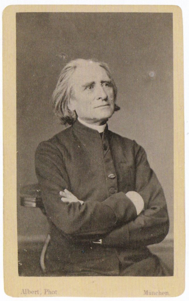 Picture in black and white taken in 1867. It represents Liszt wearing a black cassock. His arms are crossed. He is smiling. He looks toward his left. 