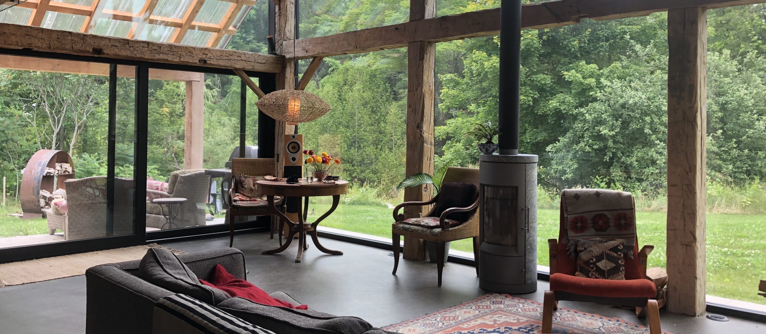 Interior of a house with a wooden structure and tall glass windows, some furniture, and a view on the nature outside.