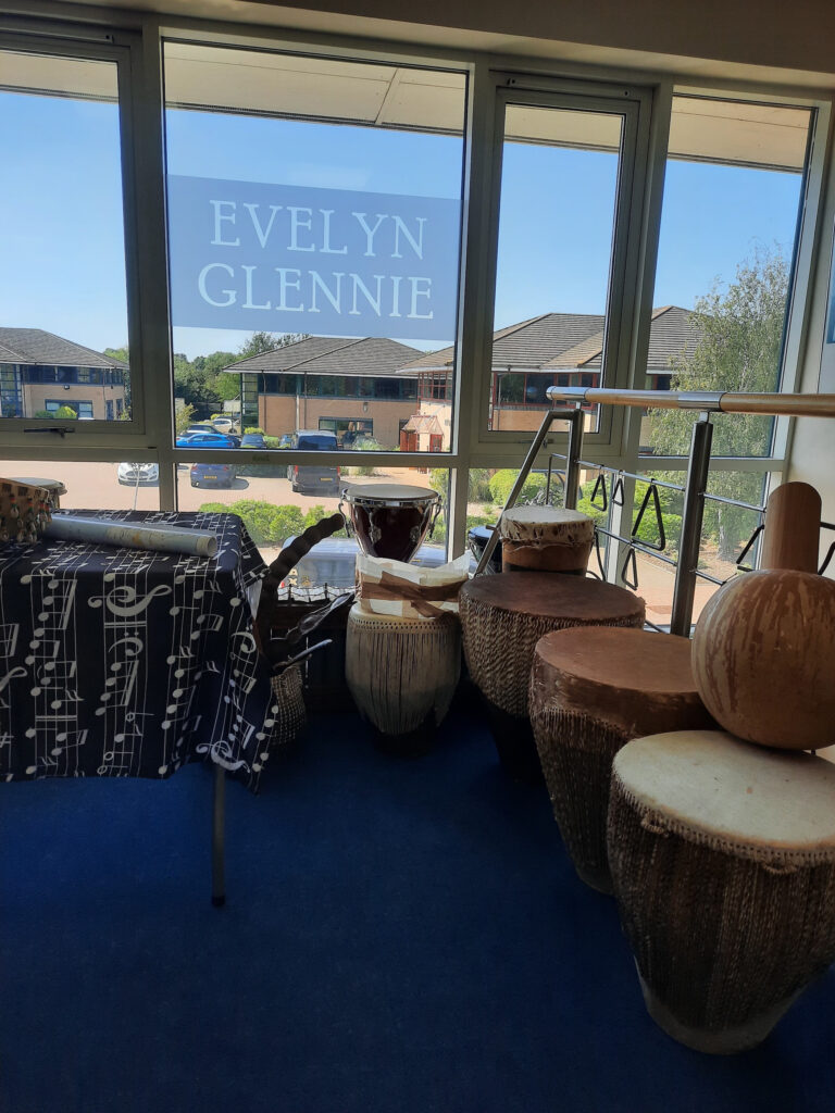 Quelques percussions sont alignées devant une fenêtre sur laquelle on peut lire l'inscription "Evelyn Glennie".